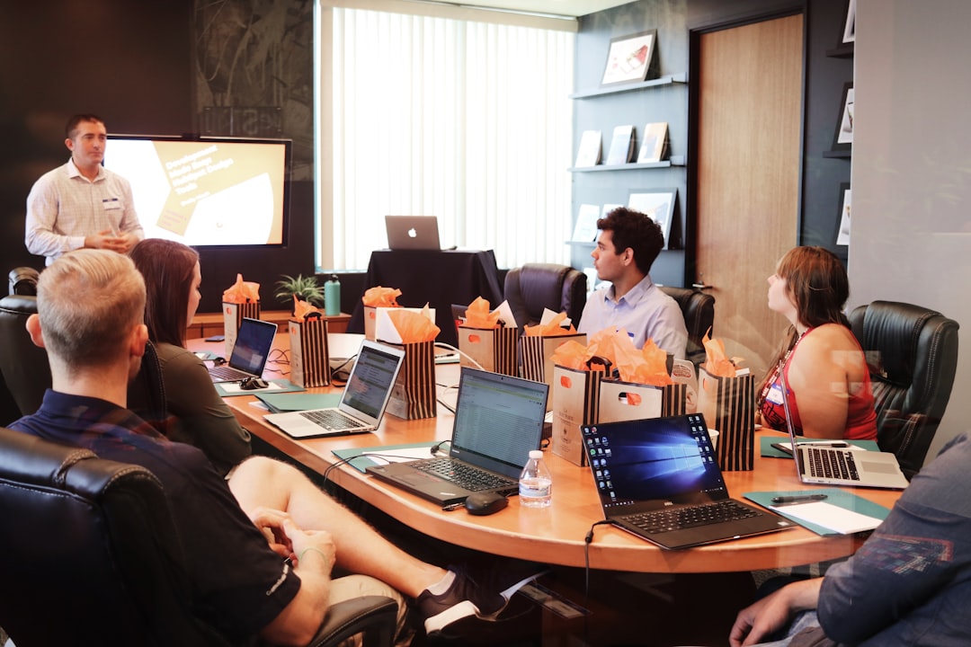 about-us man-standing-in-front-of-people-sitting-beside-table-with-laptop-computers-gmsnxqiljp4